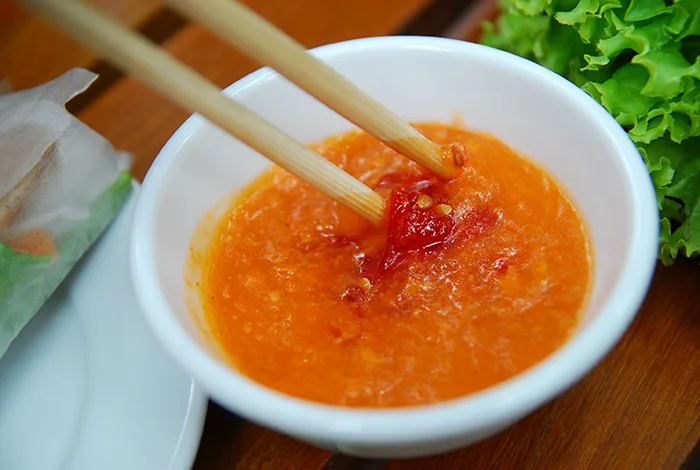 Chén nước chấm nem nướng màu cam, đũa đang chấm cuốn