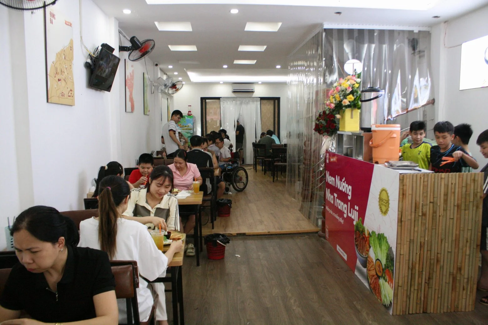 Khách ngồi ăn kín các bàn trong quán Nem Luji, quầy bếp ốp tre ở bên phải