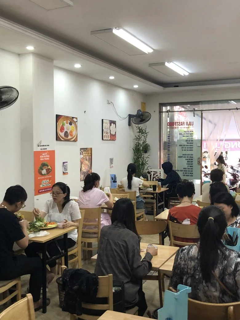 Khách ăn trưa ở dãy bàn gỗ trong quán