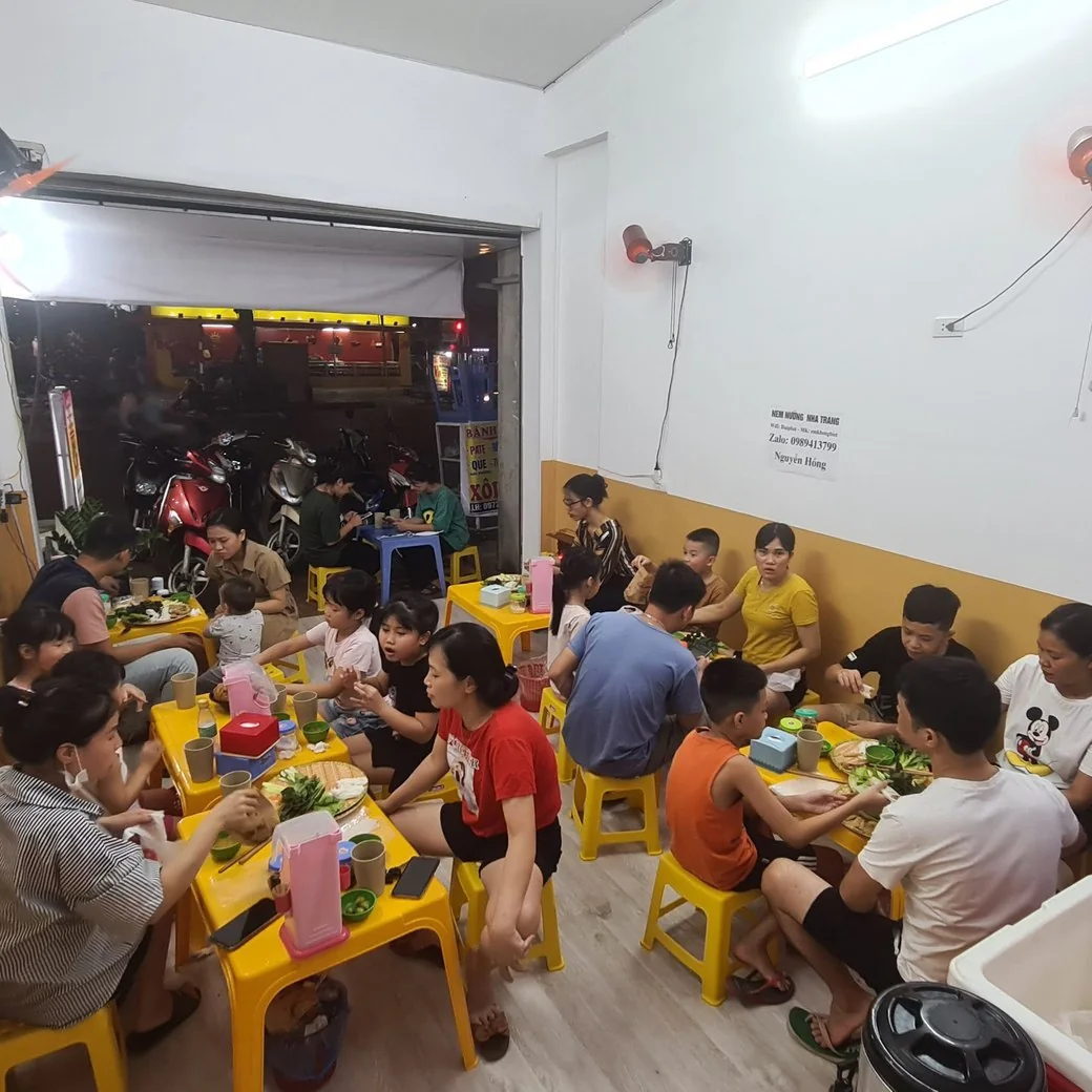 Khách ngồi ghế nhựa vàng ăn nem buổi tối, quán kín bàn